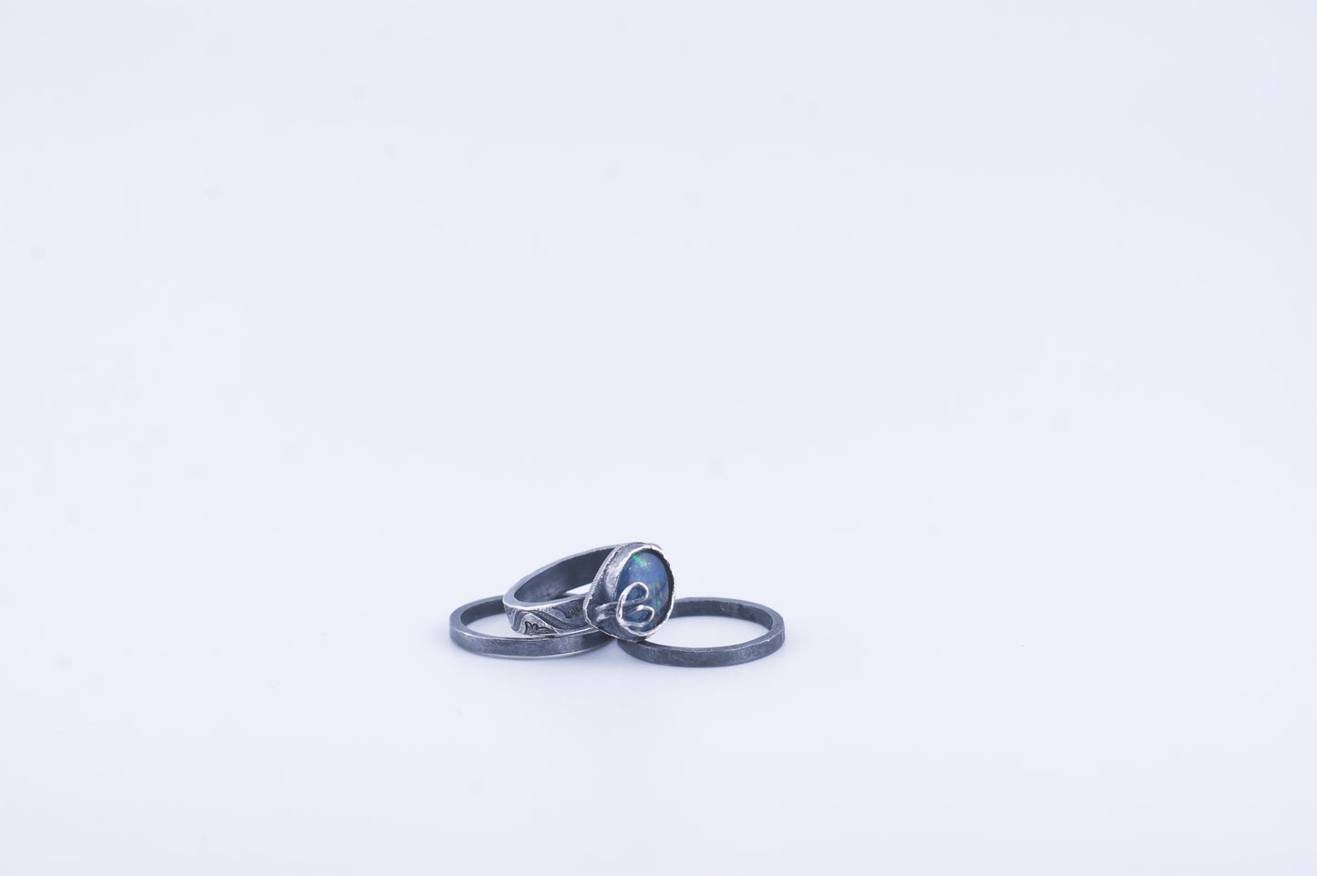 Fairy Rainbow Ring - Three patina'd sterling silver rings on a white background. One patterned band  with a set opal and beansprout prong and two thinner stack rings